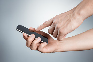 Hands holding and touching black smartphone on gray background