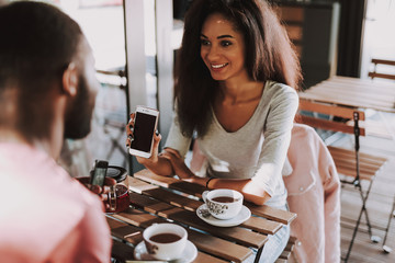 Cheerful young female sitting with phone in cafe