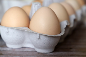 Chicken eggs in cardboard package close-up. Fresh eggs on wooden table, selective focus