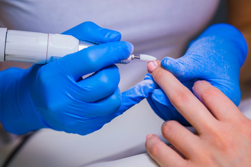 Closeup shot of master uses an electric machine to remove the nail polish during manicure in the salon. Hardware manicure. Concept of body care