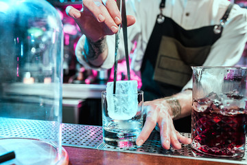 Expert barman is making cocktail at night club or bar. Glass of fiery cocktail on the bar counter against the background of bartenders hands with fire. Barman day concept