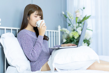 Asian woman working  on bed .She dress sweater violet colour.Morning check email internet from notebook.