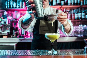 Expert barman is making cocktail at night club or bar. Glass of fiery cocktail on the bar counter against the background of bartenders hands with fire. Barman day concept