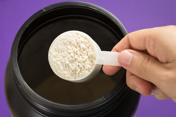 Whey Protein. Point of view of hand holding measuring scoop. Vanilla flavour. Color background: violet.