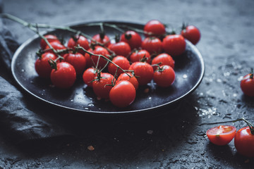 Branch of cherry tomatoes on black plate, close up. Selective focus