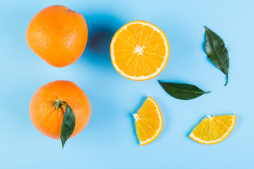 Slices of orange with leaves on blue background. Flat lay, top view.