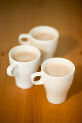 Three white cups of coffee, cocoa or latte on a wooden background on the table, close-up