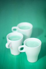 Creative photo of three cups of coffee or cocoa, green turquoise background