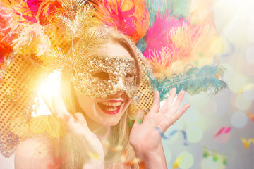 Beautiful young woman in carnival mask. Beauty model woman wearing masquerade mask at party over holiday background with magic glow. Christmas and New Year celebration. Glamour lady with perfect make