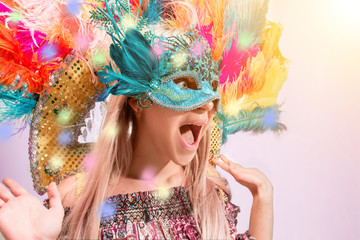 Fototapeta na wymiar Beautiful young woman in carnival mask. Beauty model woman wearing masquerade mask at party over holiday background with magic glow. Christmas and New Year celebration. Glamour lady with perfect make