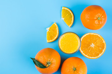 Orange juice in glass and slices of orange on blue background, top view