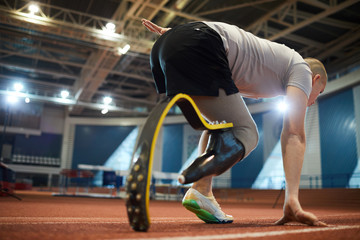 Fototapeta na wymiar Young active sportsman with handicapped leg bending over start line before competition on stadium