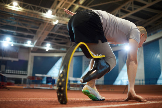 Young active sportsman with handicapped leg bending over start line before competition on stadium