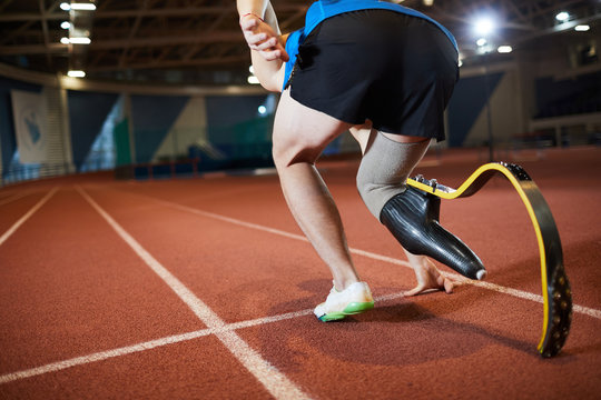Back view of paralympic sportsman with handicapped leg bending by start line on stadium ready to go