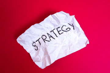 Word Strategy written on Crumpled paper on red background