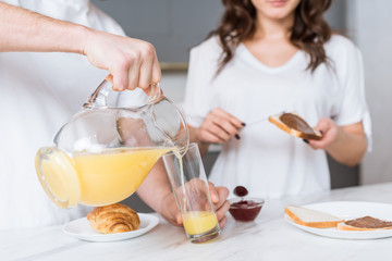 Obraz premium selective focus of man pouring orange juice in glass near girlfriend in kitchen