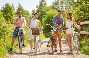 people, technology and lifestyle concept - happy couple with bicycles and smartphone at country in summer