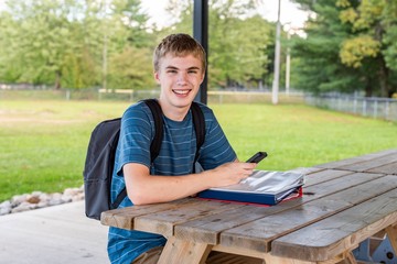 Happy teenager studying for a test outdoors with the help of his phone.