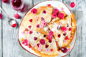 Idea for Valentine's Day surprise gift. Cute pancakes crepes with berry sauce and heart shaped cutouts. Romantic valentine breakfast. On wooden table, with fresh raspberries. Copy space