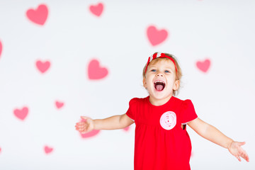 Little blonde girl in red dress with red wreath with heatrs on the white background with pink hearts on the St. Valentine's day