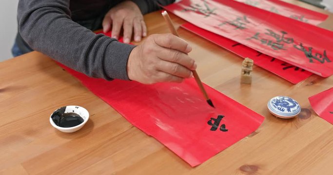 Man write chinese calligraphy for lunar new year, words mean happy new year