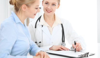 Doctor and patient talking in hospital office while sitting at the desk. Health care and client service in medicine