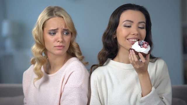 Hungry woman on diet looking at her skinny friend enjoying tasty cake, envy