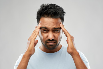 people, health problem and stress concept - unhappy indian man suffering from headache over grey...