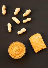 Bowl of peanut butter, unshelled peanuts on a dark black surface, top view. Close-up.