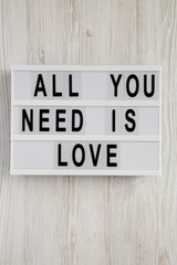 Modern board with text 'All you need is love' on a white wooden background, top view. From above, flat lay, overhead.
