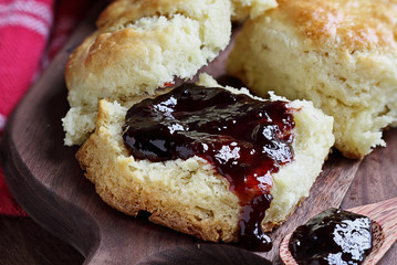 Homemade berry preserves dripping over fresh buttermilk southern biscuits or scones over rustic cutting board background.
