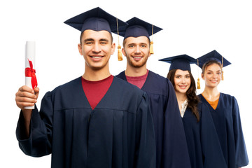 education, graduation and people concept - group of happy graduate students in mortar boards and bachelor gowns with diploma over white background