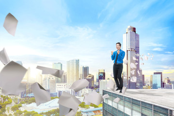 Handsome asian businessman standing with flying paper on the building rooftop