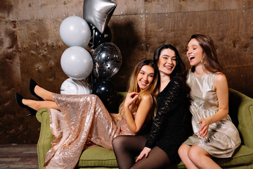 Portrait of group three young attractive pretty women have fun and relaxing on party with balloons wearing evening sparkling dresses and talkinf to each other