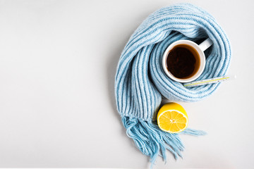 Tea cup with thermometer, blue scarf, pills and lemon on gray background. Flu season, disease.