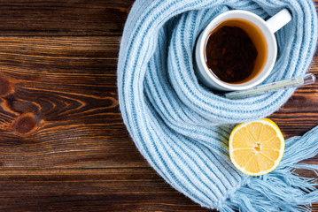 Tea cup with thermometer, blue scarf and lemon on wooden background. Flu season, disease.