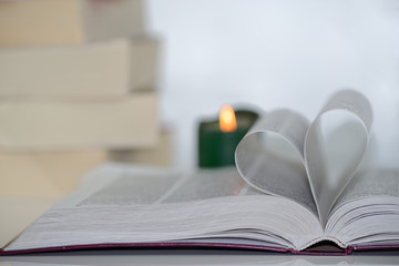 Heart shape from paper book against blurry green candle and pile of books