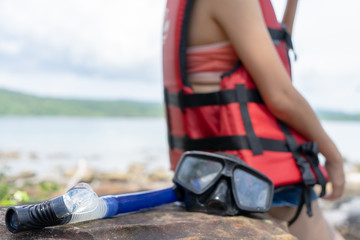 Diving mask and Snorkel Gear on beach stone with woman wearing life jacket relaxing on summer holidays. .Beach vacation snorkel girl snorkeling with mask.