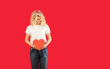 beautiful young emotional girl with a red heart in her hands is standing on an isolated red background.Valentine's Day.