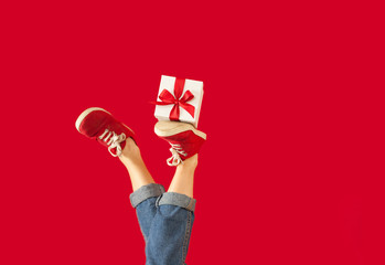 feet with a gift for the holidays on an isolated red background, a girl with a gift, giving gifts, discounts. Valentine's Day.