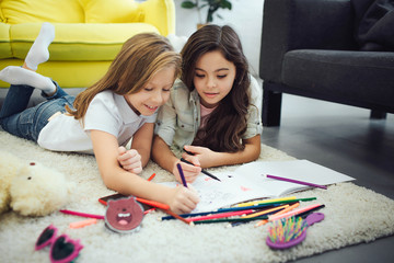 Two busy teenagers lying carpet floor in room. They drawing.