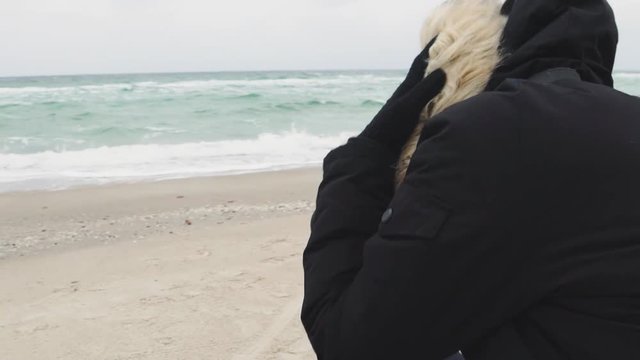 Young beautiful woman taking pictures of the sea on a cold winter day. Slow motion 