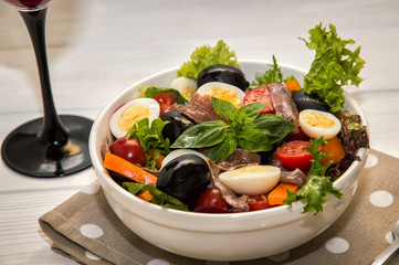 Close up, macro. French dinner served with red wine. Traditional niçoise (nicoise) salad in a white plate on a polka dot napkin.