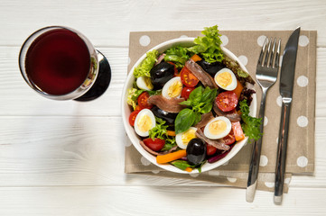 Top view. French niçoise (nicoise) salad served with red wine. White wooden background. Copy space.