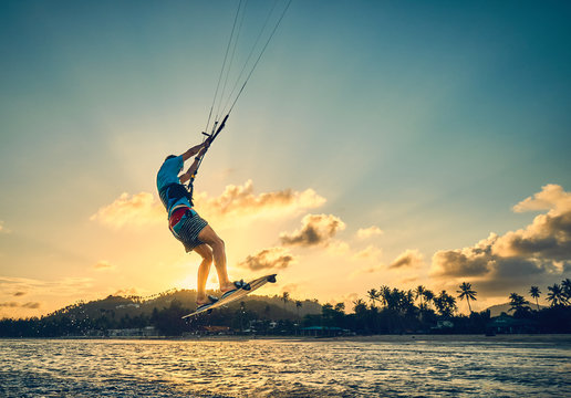 Young man kite boarder jumps over the sea at sunset          