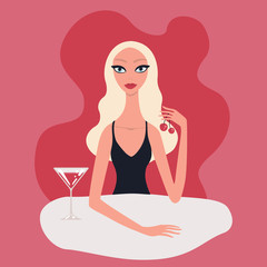 Hot beautiful young blond woman with perfect make-up red lipstick blue eyes wearing black evening dress sitting at table drinking cocktail with cherries Aperitives Alcoholic drinks Restaurant Cafe.