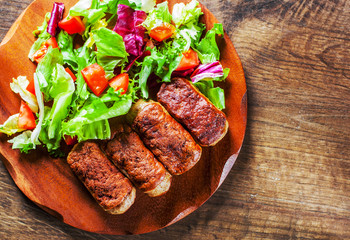 roasted sausages and various fresh mix salad leaves with tomato in plate on wooden table background