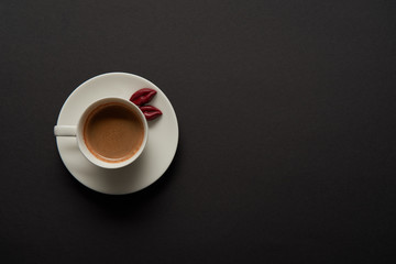 top view of cup of coffee with chocolate lips on saucer on black background