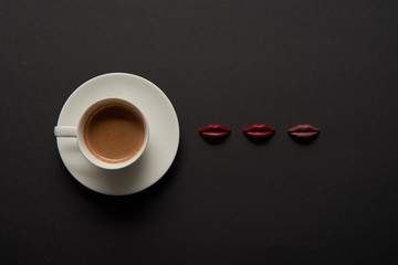 top view of cup of coffee near chocolate lips on black background