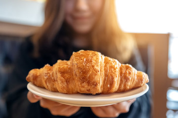 An asian woman holding and showing a dish of fresh croissant